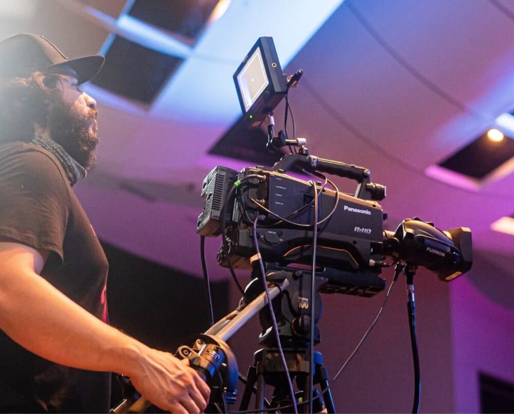 Broadcast professional operating a Panasonic camera during a live event.