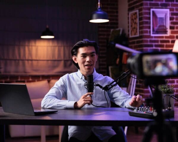 Broadcaster recording a live tutorial with a microphone and camera in a studio setting.