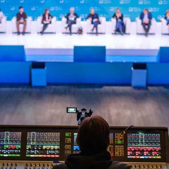 Camera operator controlling equipment while filming a live event panel discussion.