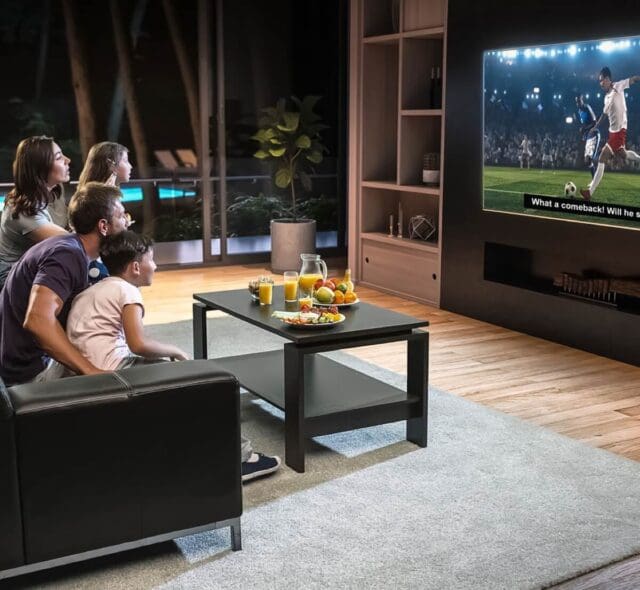 A family watching a sports game on TV, celebrating a win while enjoying drinks and snacks.