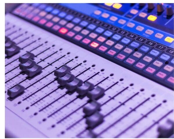 Close-up of a mixing desk with sliders, buttons, and colourful controls in a studio setting.