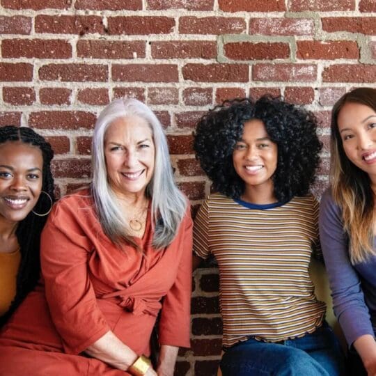 Group of multicultural women smiling together against a brick wall.