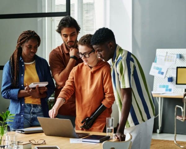 Group of people collaborating in an office space, working on a laptop together.