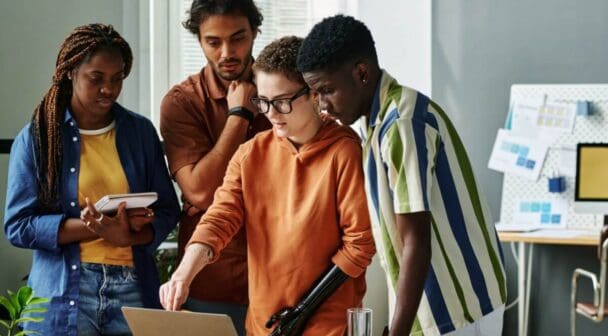 Group of people collaborating in an office space, working on a laptop together.