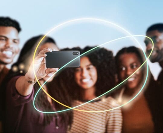 Group of people taking a selfie with a smartphone, surrounded by colourful light trails.