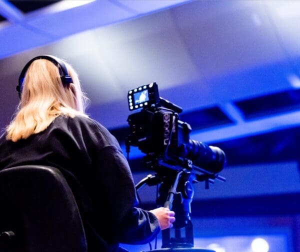Person operating a broadcast camera with headphones in a studio or event venue.
