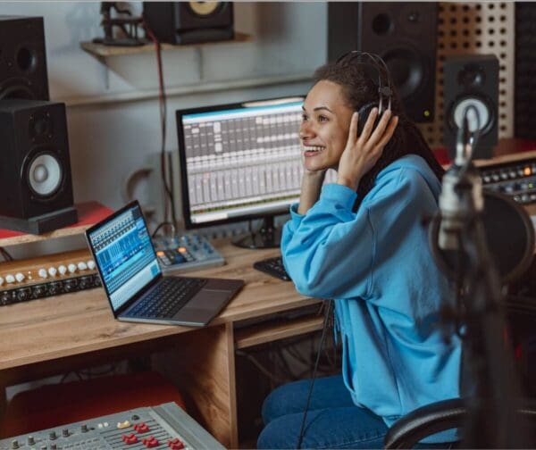 Presenter wearing headphones and working in a broadcast studio with audio equipment and monitors.