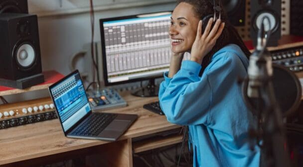 Presenter wearing headphones and working in a broadcast studio with audio equipment and monitors.