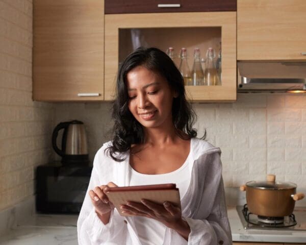 Smiling woman using a tablet in her kitchen with a kettle and pot in the background.